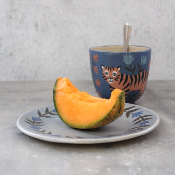 ensemble tasse et sous tasse artisanales en grès décorées à la main. Illustration tigre et fleur sur fond bleu roi.